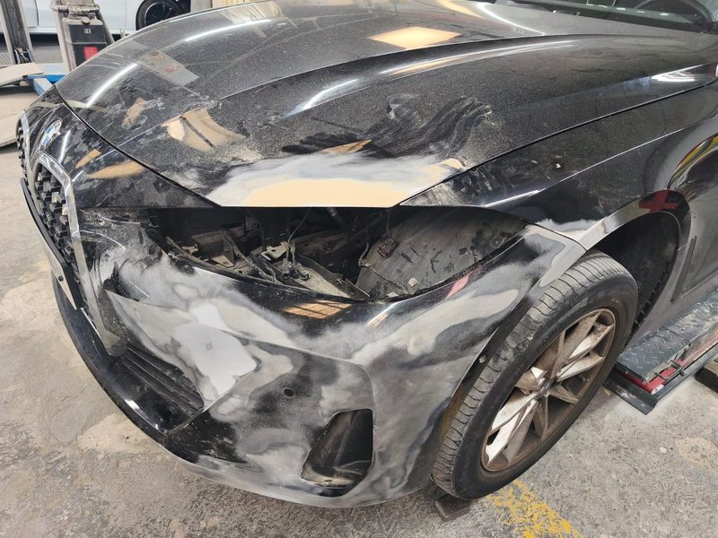 Frontal d’un cotxe fosc amb el para-xocs en procés de reparació